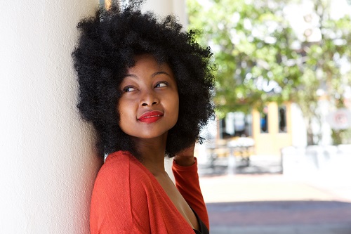 young woman outside leaning against wall daydreaming